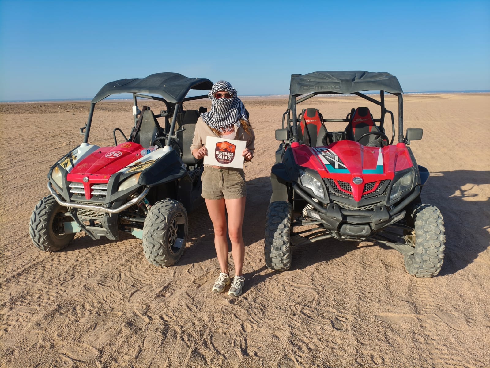 Guest standing between two buggies holding the Hurghada Safari sign on a buggy tour in Hurghada